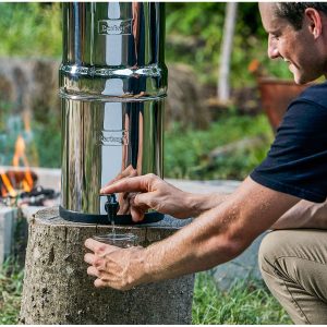 Berkey waterfilter op houtblok, man tapt water, kampvuur