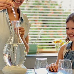 La mère verse des gouttes de minéraux dans la carafe MAYU Swirl, l'enfant porte des lunettes.