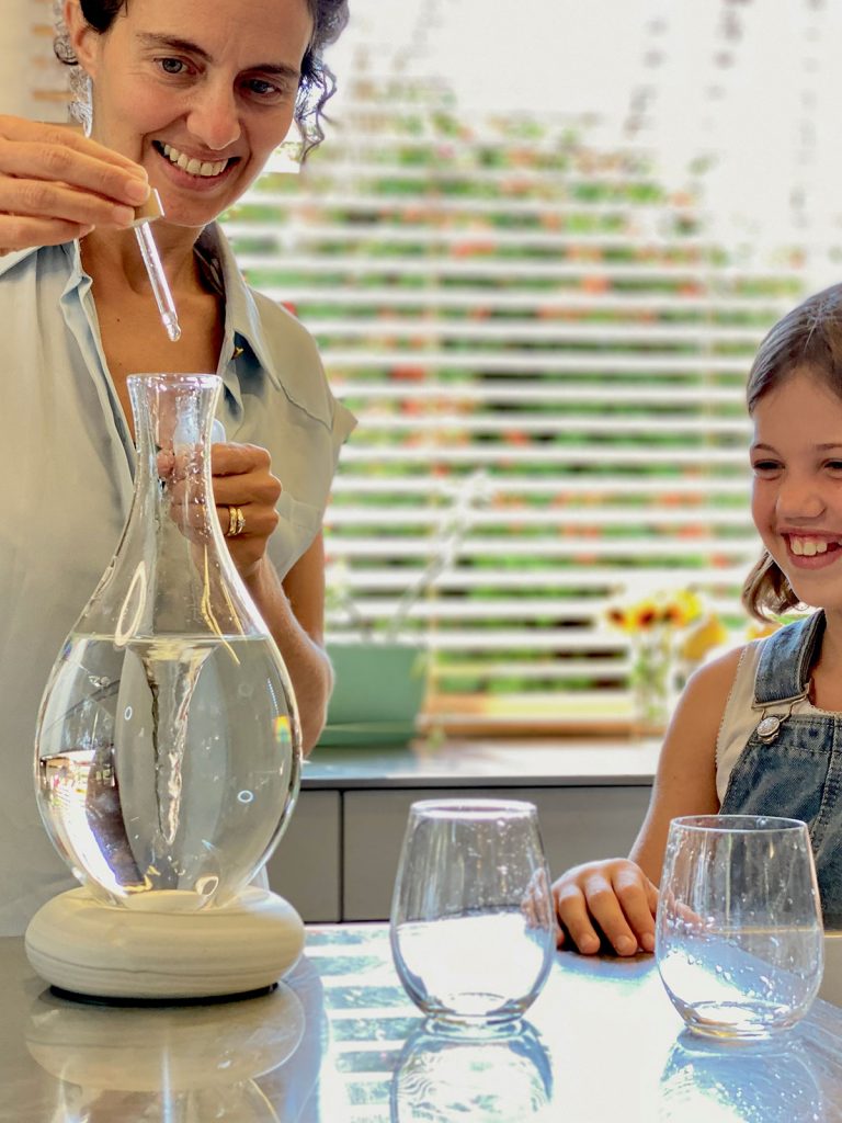 La mère verse des gouttes de minéraux dans la carafe MAYU Swirl, l'enfant porte des lunettes.