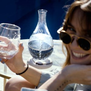 MAYU Swirl au bord d'une piscine, une femme avec des lunettes de soleil sourit, un verre à la main