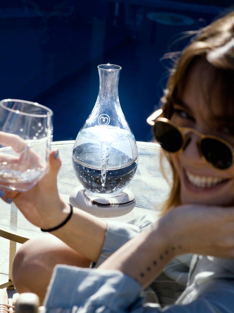 MAYU Swirl junto a la piscina, mujer con gafas de sol sonríe, vaso en mano