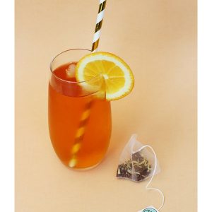 Glas kalter Kindertee Mangos Tea Tub mit Eiswürfeln, Strohhalm und Zitronenscheibe. Teebeutel neben dem Glas